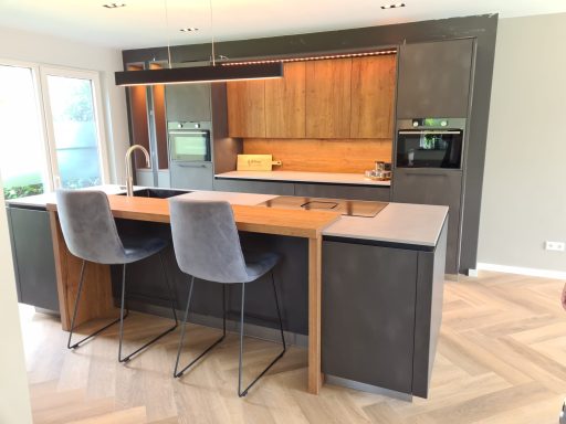 Moderne keuken met houtaccenten, kookeiland en twee hoge stoelen.